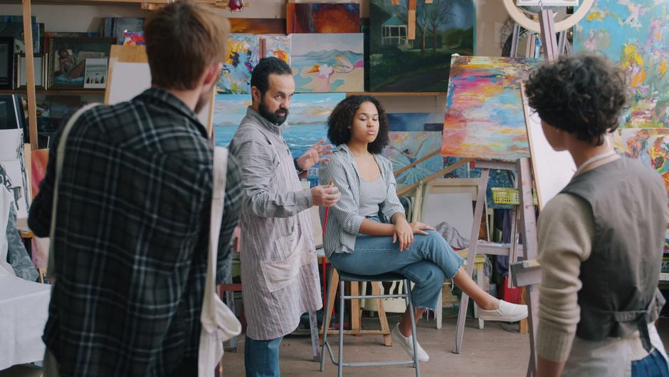 Art instructor guiding students in a creative studio with vibrant paintings.